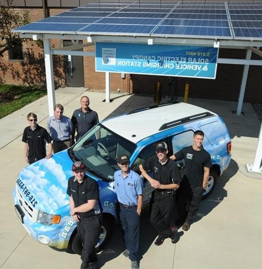 汽车技术专业的学生站在项目的太阳能电池板和电动汽车充电站前